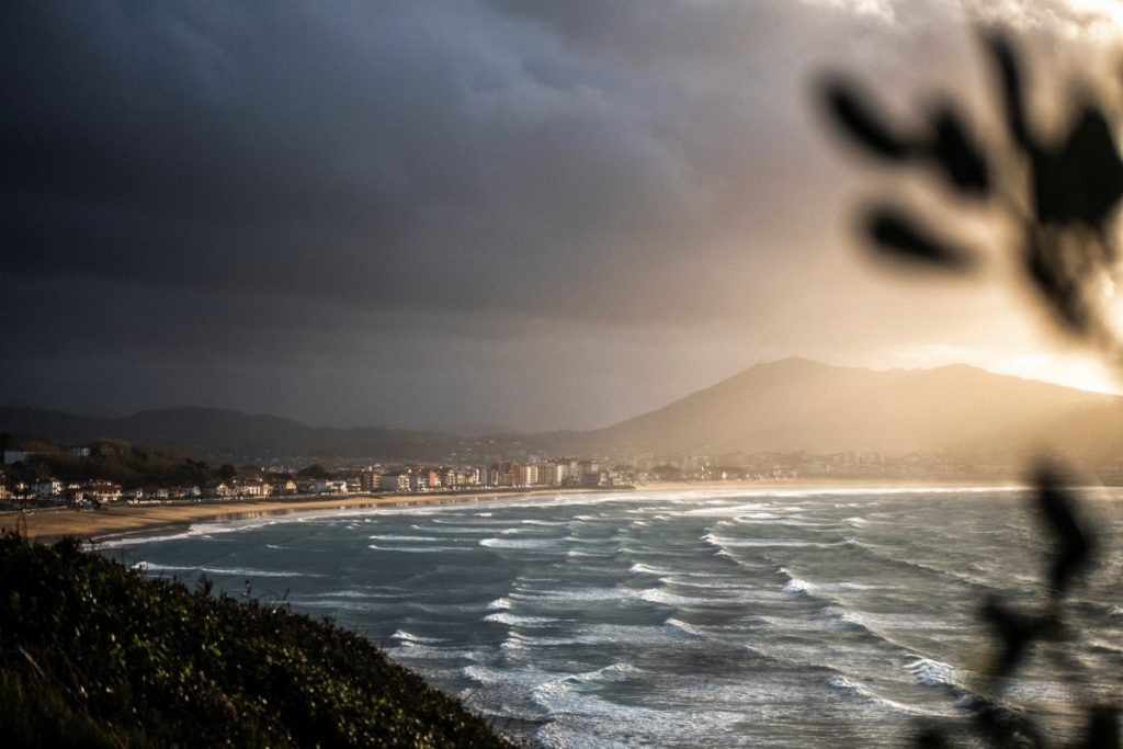 vue sur le littoral d'hendaye au pays basque. une mer forte et puissante fait claquer les vagues sur la plage et le soleil perce le ciel menaçant